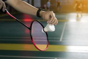 Badminton player holds white cream shuttlecock and racket in front of the net before serving it to another side of the court, soft and selective focus on shuttlecock. photo