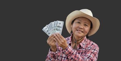 una anciana asiática aislada sostiene billetes de banco en dólares estadounidenses en la mano con una hermosa sonrisa en su rostro felizmente con senderos recortados. foto