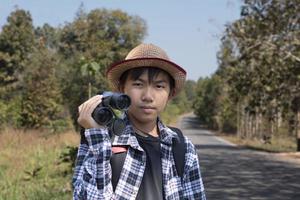 un niño asiático está usando binoculares para observar aves en el bosque tropical durante el campamento de verano, idea para aprender criaturas y animales salvajes e insectos fuera del aula. foto