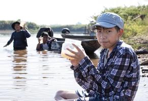 un joven asiático sostiene un tubo transparente que tiene agua de ejemplo dentro para hacer el experimento y la medición del nivel de ph mientras su proyecto escolar trabaja con sus amigos detrás del río donde vivía. foto