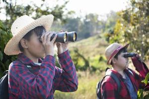 Asian boys are using binoculars to do the birds' watching in tropical forest during summer camp, idea for learning creatures and wildlife animals and insects outside the classroom. photo