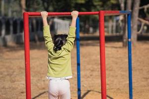 Cute asian girl smile play climb the bar on school or kindergarten yard or playground. Healthy activity children. Little girl climbing outdoors at playground. Child playing on outdoor playground. photo