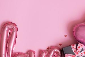 Fragment of foil baloon in love and heart shape with gift box on pink background copy space. Valentines Day concept photo