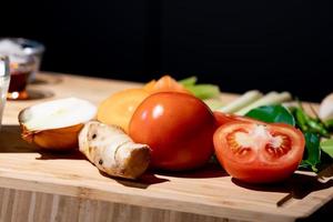 Tomato and sliced half of tomato beside it with onion and galangal, on wood plate in studio light with dark theme. photo