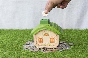 Mock up house with coins on grass floor and hand putting money coin. photo