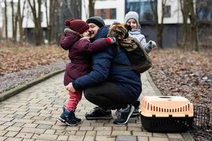 Father and daughters with cat in travel pet plastic cage carriage outdoor at park. photo