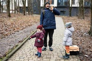 Father and daughters with cat in travel pet plastic cage carriage outdoor at park. photo