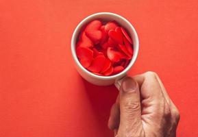 man hand holding white cup full of hearts on red background , valentines day concept photo