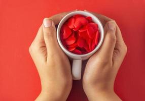 woman hand holding white mug full of hearts on red background, valentines day concept photo