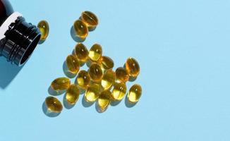 Yellow capsules with fish oil on a blue background, top view photo