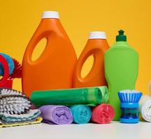 Orange plastic bottles with liquid products and garbage bags on a white table, yellow background photo