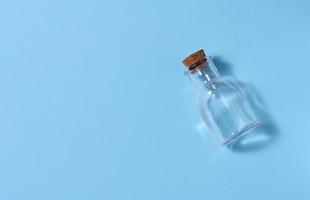 Empty glass bottle with cork on blue background, top view photo