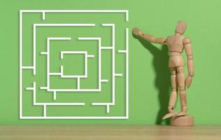 Wooden figurine of a mannequin and a labyrinth on a green background. Solution search concept photo