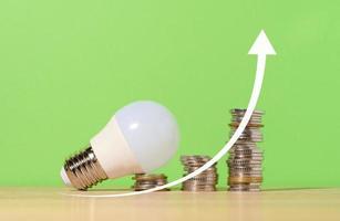 una pila de monedas y una lámpara de cristal sobre un fondo verde, flecha arriba. el concepto del crecimiento de nuevas ideas en los negocios, altos ingresos. aumento de los precios de la electricidad foto