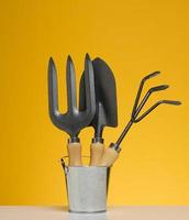 Miniature garden tools in a metal bucket on a yellow background photo