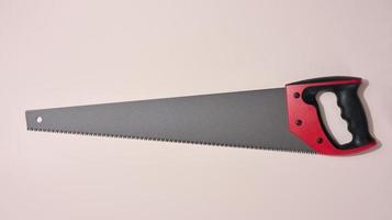 New hand saw with a rubber red handle on a beige background, photo