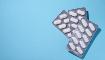 Oval white pills in a gray blister pack on a blue background, top view photo