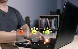 a businessman using computer laptop and touching the virtual screen on the happy smile face icon to give satisfaction in service.rating very impressed.Customer service and Satisfaction concept photo