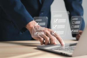 Businessman working at laptop computer and digital documents with questionnaire with checkboxes. Survey form concept. photo