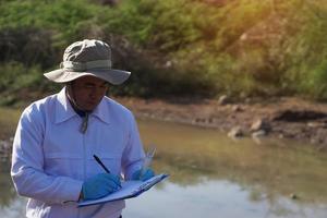 Asian man environment researcher holds tube of sample water to inspect from the lake. Concept, explore, analysis water quality from natural source. Ecology field research. photo