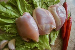 primer plano de filete de muslo de pollo crudo en una tabla de cortar con lechuga, chiles rojos y ajos. sin piel y sin espinas. muslo de pollo fresco y orgánico. vista superior foto