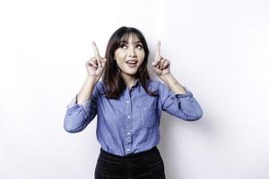 Excited Asian woman wearing blue shirt pointing at the copy space on top of her, isolated by white background photo