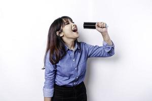 Portrait of carefree Asian woman, having fun karaoke, singing in microphone while standing over white background photo