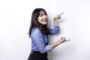 mujer asiática emocionada con pantalones azul apuntando al espacio de copia a su lado, aislada por fondo blanco foto