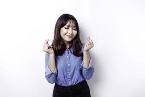 A happy young Asian woman wearing a blue shirt feels romantic shapes heart gesture expresses tender feelings photo