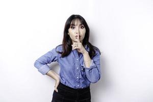 Portrait of a young Asian woman tell be quiet, shushing with serious face, hush with finger pressed to lips, isolated by white background photo