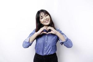 A happy young Asian woman wearing a blue shirt feels romantic shapes heart gesture expresses tender feelings photo