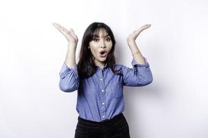 Shocked Asian woman wearing blue shirt pointing at the copy space on top of her, isolated by white background photo
