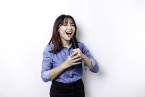 Portrait of carefree Asian woman, having fun karaoke, singing in microphone while standing over white background photo
