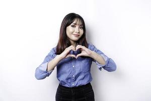 una joven asiática feliz con una camisa azul siente formas románticas gesto de corazón expresa sentimientos tiernos foto