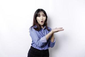 Shocked Asian woman wearing blue shirt pointing at the copy space beside her, isolated by white background photo