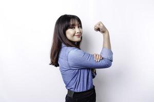 mujer asiática emocionada con una camisa azul que muestra un gesto fuerte levantando los brazos y los músculos sonriendo con orgullo foto