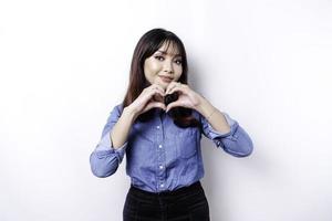 A happy young Asian woman wearing a blue shirt feels romantic shapes heart gesture expresses tender feelings photo