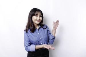 Excited Asian woman wearing blue shirt pointing at the copy space beside her, isolated by white background photo