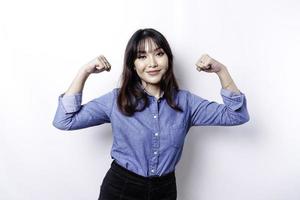 mujer asiática emocionada con una camisa azul que muestra un gesto fuerte levantando los brazos y los músculos sonriendo con orgullo foto