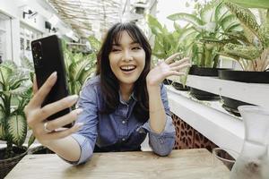 A happy Asian woman in a restaurant, wearing a blue shirt and holding her phone photo