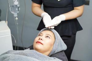 Primer espectáculo de enfermera de belleza de crema exfoliante facial en las manos antes de hacer un masaje facial con exfoliante facial orgánico en la cara del cliente. foto