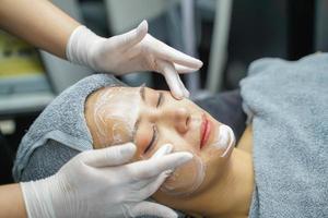 mujer joven belleza en toalla haciendo masaje facial con exfoliante facial orgánico.