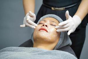 mujer joven belleza en toalla haciendo masaje facial con exfoliante facial orgánico. foto