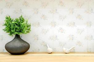 Ornamental plants in small black ceramic vase put on wooden table front of flowers pattern tile in the toilet. photo