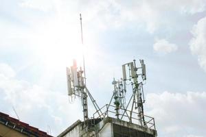 Communication tower with antennas on the top of building on bright blue sky with cloud background. photo