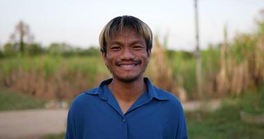 ritratto di un asiatico giovane contento contadino uomo guardare a telecamera e sorridente con un' terreni agricoli sfondo. agricoltura agricoltura concetto. lento movimento. video