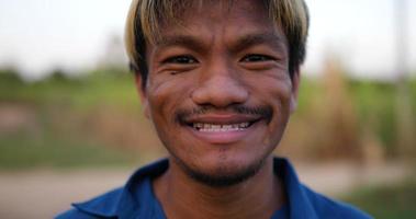 retrato próximo de um jovem fazendeiro feliz asiático olhando para a câmera e sorrindo com um fundo de terras agrícolas. conceito de agricultura agrícola. câmera lenta. video