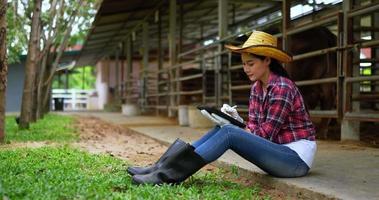 femme asiatique attrayante éleveur de bétail agricole utiliser un stylo numérique écrire sur une tablette tout en vérifiant les animaux dans la ferme video