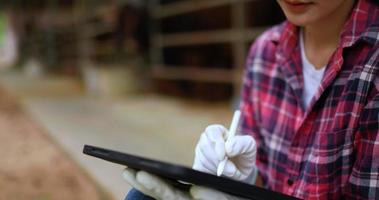 feche a mão de uma atraente criadora de gado agrícola asiática, use caneta digital para escrever no tablet enquanto verifica os animais na fazenda video