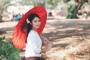 mujer asiática con vestido típico tailandés con paraguas rojo, traje tailandés foto